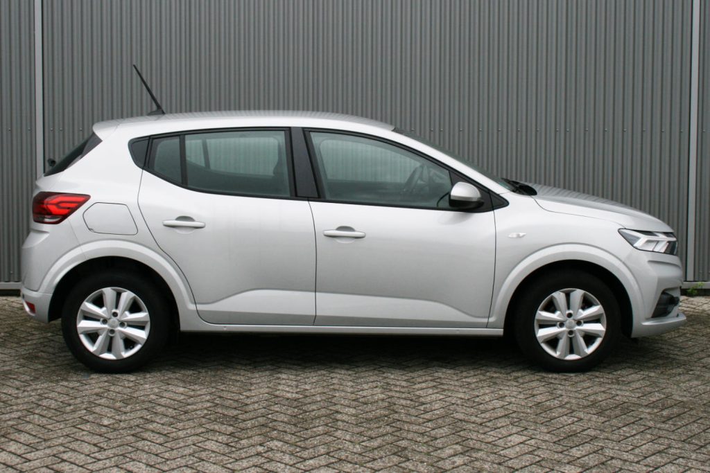 Zilveren vijfdeurs hatchback geparkeerd voor grijze metalen wand