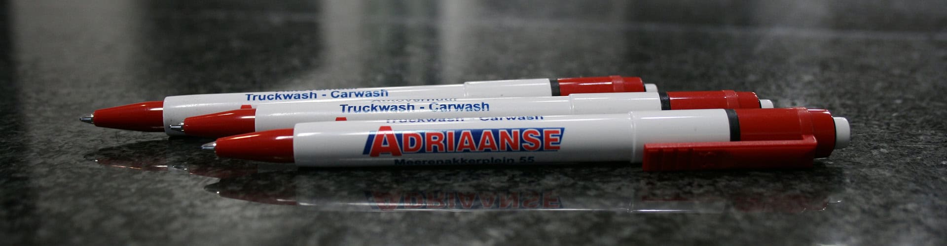 Witte en rode pennen met Adriaanse-logo op tafel