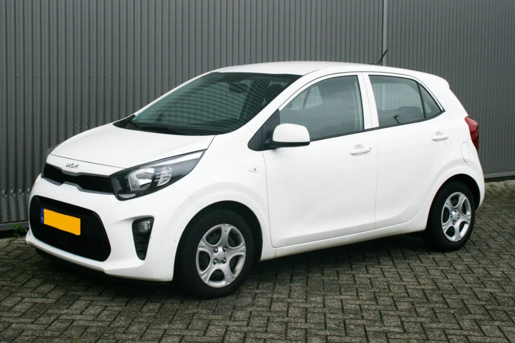 Witte Kia Picanto geparkeerd voor grijze metalen wand