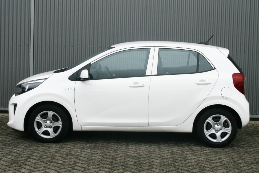 Witte vijfdeurs hatchback geparkeerd voor metalen wand