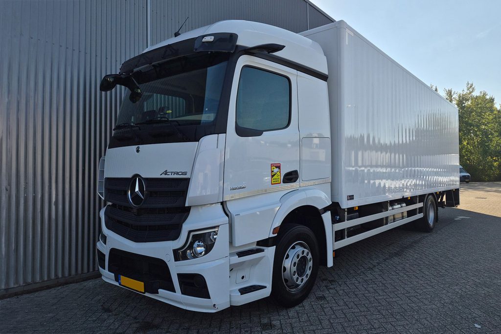 Witte Mercedes-Benz Arocs bakwagen naast bedrijfsgebouw