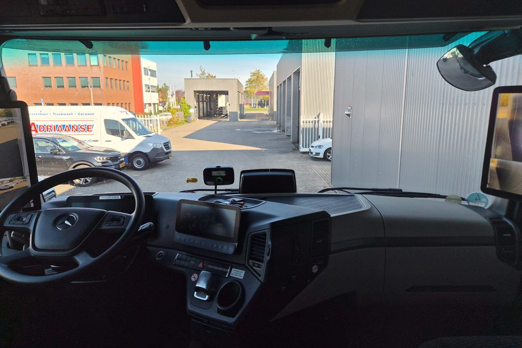 Uitzicht vanuit vrachtwagencabine op bedrijfs terrein met bestelbus