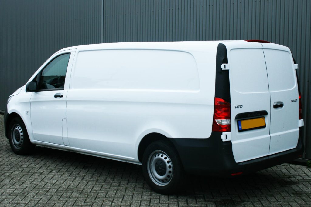 Witte bestelwagen geparkeerd voor een grijze loods
