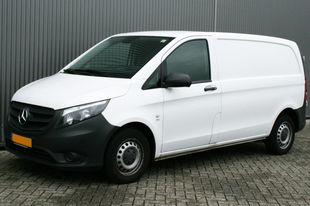 Witte Mercedes-Benz bestelwagen geparkeerd voor grijze metalen wand