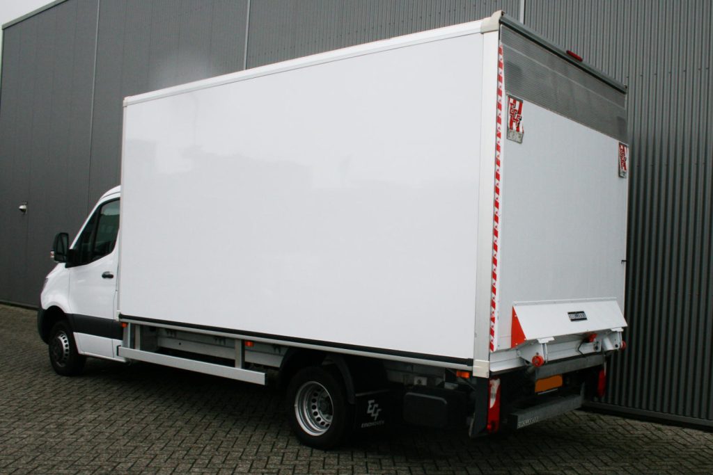 Witte bakwagen met laadklep bij bedrijfsgebouw