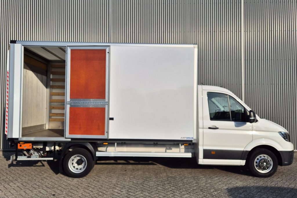 Witte bakwagen met geopende laadruimte naast metalen gevel