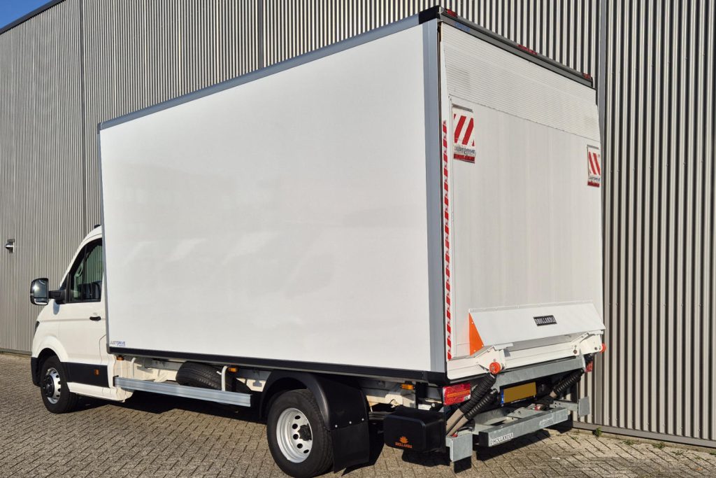 Witte bakwagen met laadklep naast bedrijfsgebouw